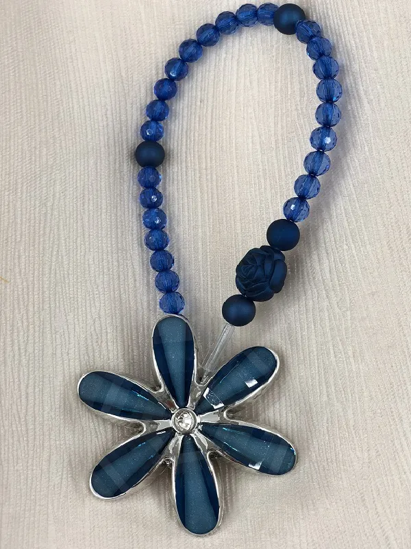 A delicate blue floral tieback with faceted crystal petals and beaded cord, resting on a textured beige fabric background, evoking coastal elegance and refined window decor.