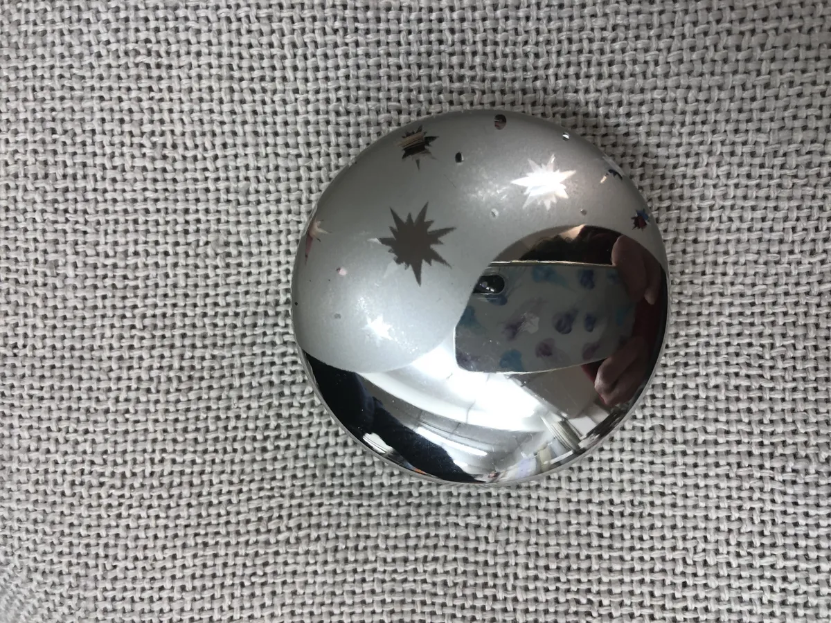 Металлический подхват с гравировкой звёзд лежит на светлой ткани. В отражении видны звёзды и луна. Ночная атмосфера, уют и роскошь. Интерьер в стиле минимализм с акцентом на небесную тематику.