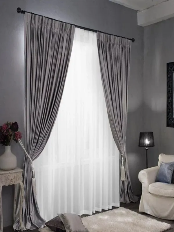 Luxurious charcoal velvet curtains with sheer white overlay, elegantly tied back in a modern gray living room with plush rug and vintage side table.