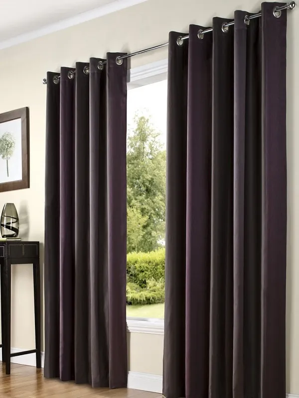 Velvet twilight grommet curtains elegantly draped over a large window, casting deep shadows and framing a lush green garden view in a modern living room.