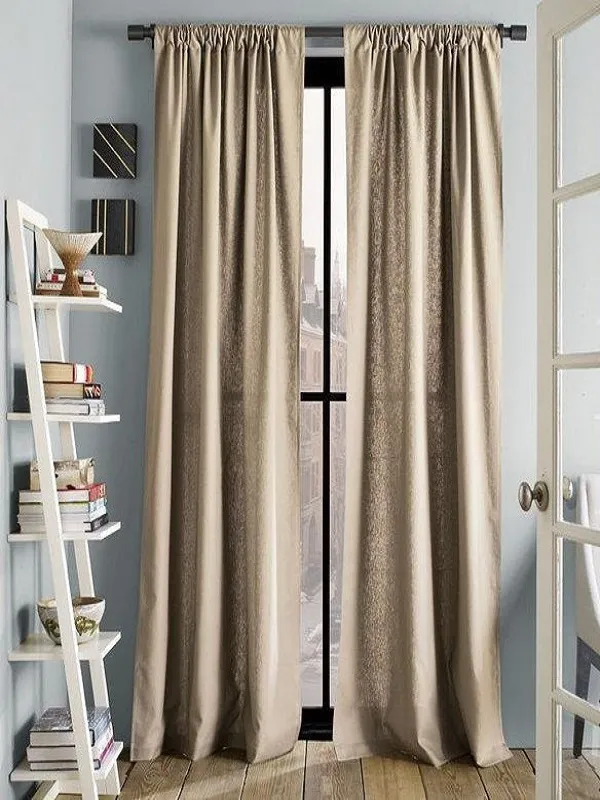 Тёплые бархатные шторы в золотисто-бежевом оттенке висят на окне с видом на город, рядом стоит белая лестница с книгами, настроение уютное и элегантное.