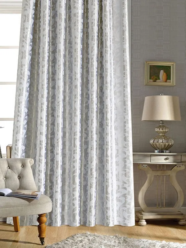 Шторы с тонким узором в серых тонах висят на окне, мягко рассеивая свет. В комнате — кресло, столик с лампой и картина на стене. Интерьер уютный, светлый, с деревянным полом и ковром. Воздух наполнен спокойствием и утончённостью.