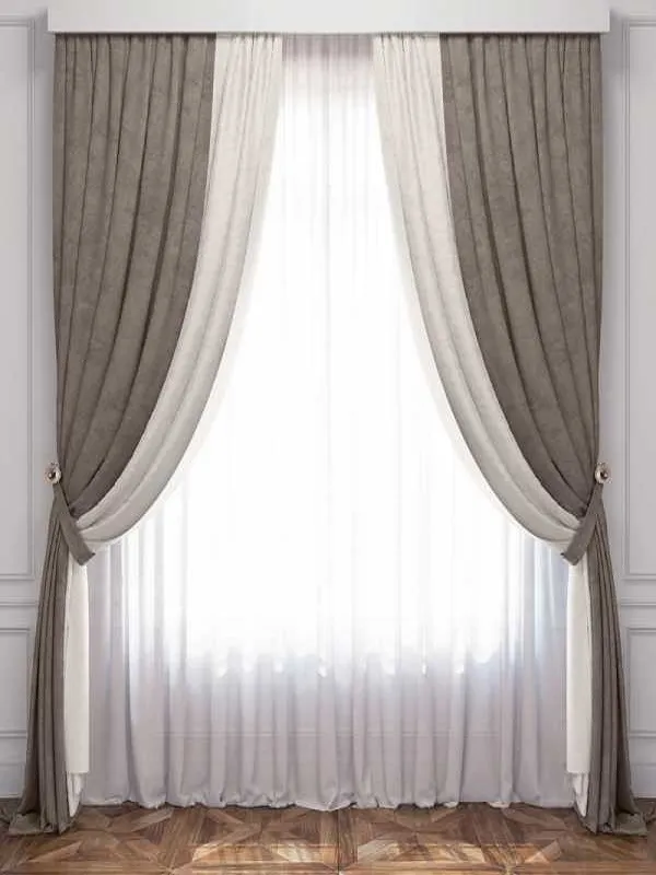 Роскошный комплект штор из бархата и тюля в серо-бежевых тонах, висит на классическом окне с белыми панелями. Свет проникает сквозь тюль, создавая нежные блики. Подхваты аккуратно держат складки. На полу — деревянный паркет в шахматном узоре. Всё выглядит утончённо и уютно.