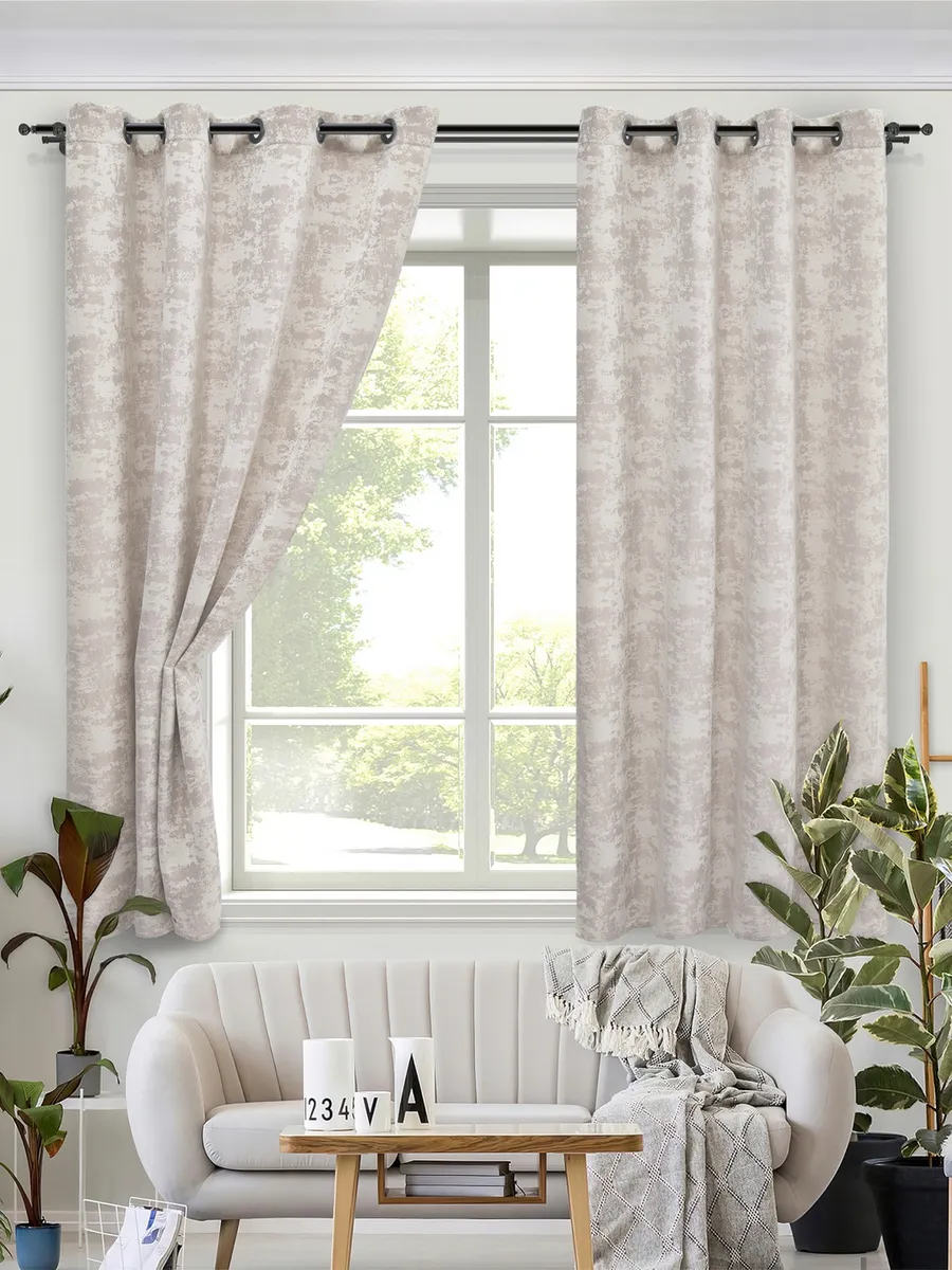 Светлые шторы на люверсах висят на окне, мягко фильтруя дневной свет. В комнате — белый диван, деревянный столик и зелёные растения. Интерьер выглядит уютным, современным и спокойным. На заднем плане — зелёный сад за окном.