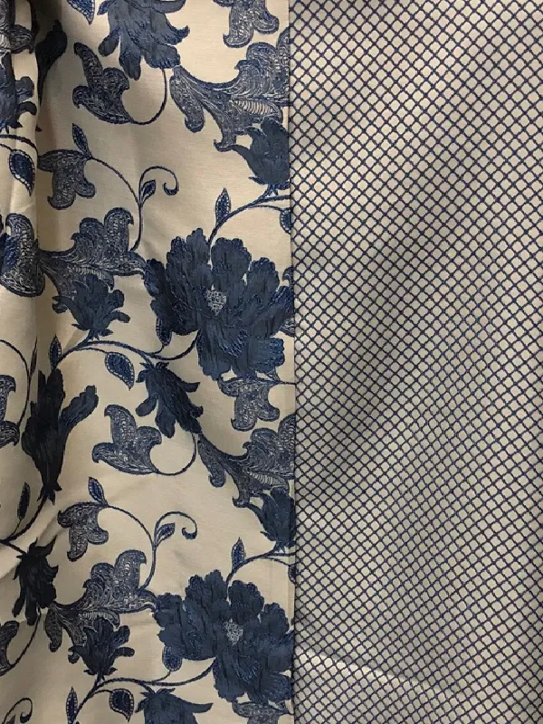 Ткань с тонким флоральным узором в синих тонах на светлом фоне, висит на окне, пропуская рассеянный свет, создаёт уютную и элегантную атмосферу в интерьере.