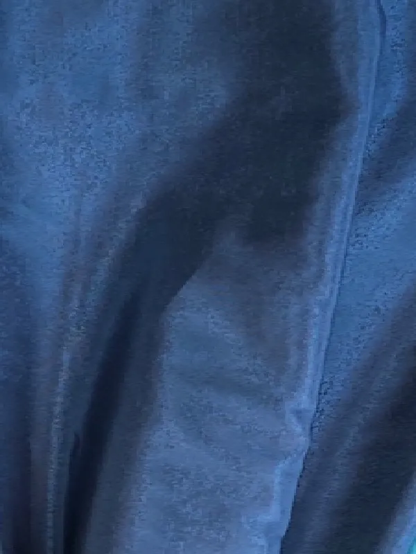 Тафта тёмно-синего оттенка с глубокими складками в элегантной комнате. Свет падает на ткань, подчёркивая её гладкость и сияние. Интерьер выглядит утончённо и роскошно.