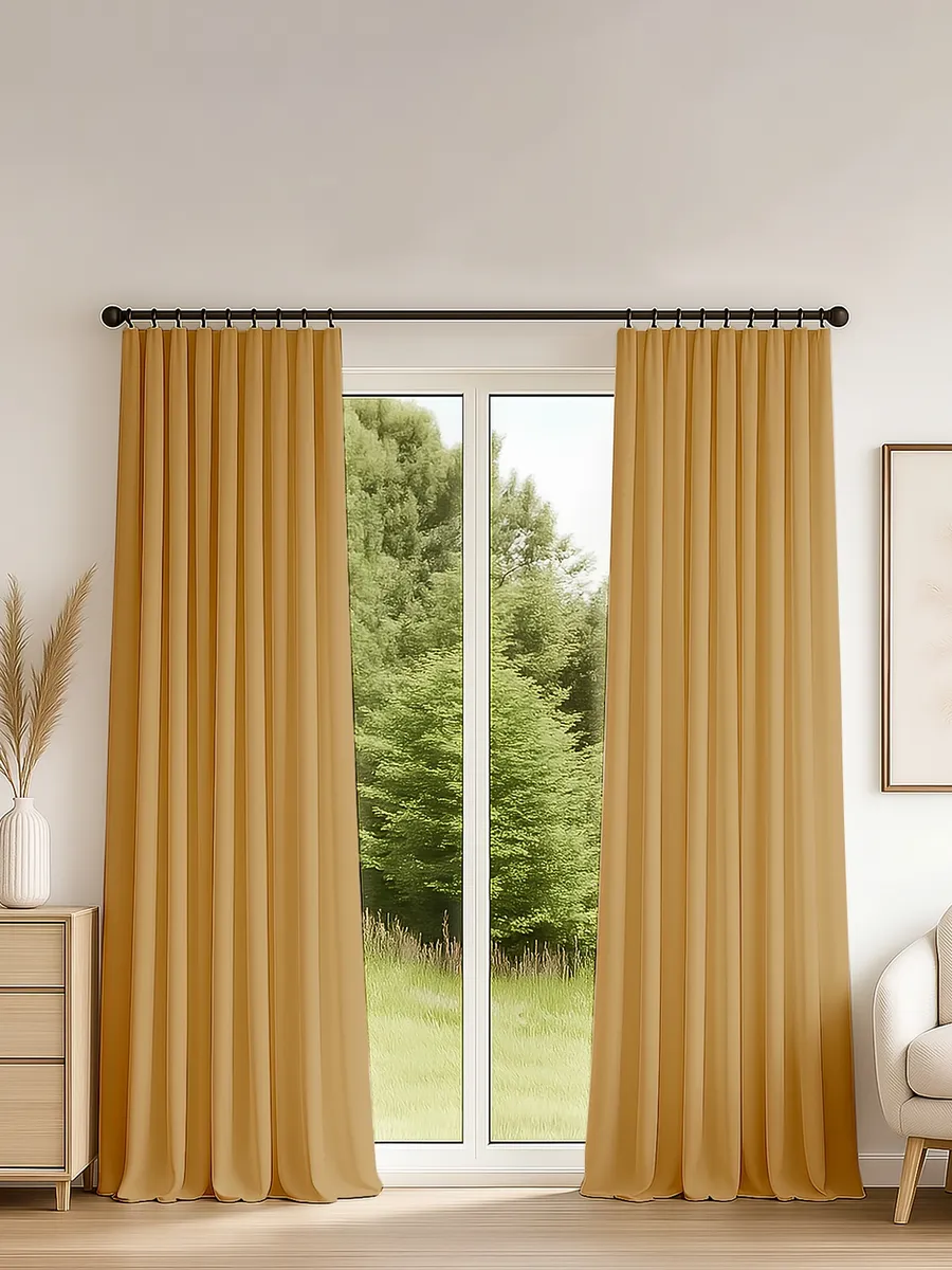 Тяжёлые шторы на ленте в тёплом золотистом оттенке, мягко драпируются на окне с видом на зелёный сад. Интерьер в нейтральных тонах, уютное освещение, деревянный пол, кресло и ваза с сухими растениями.