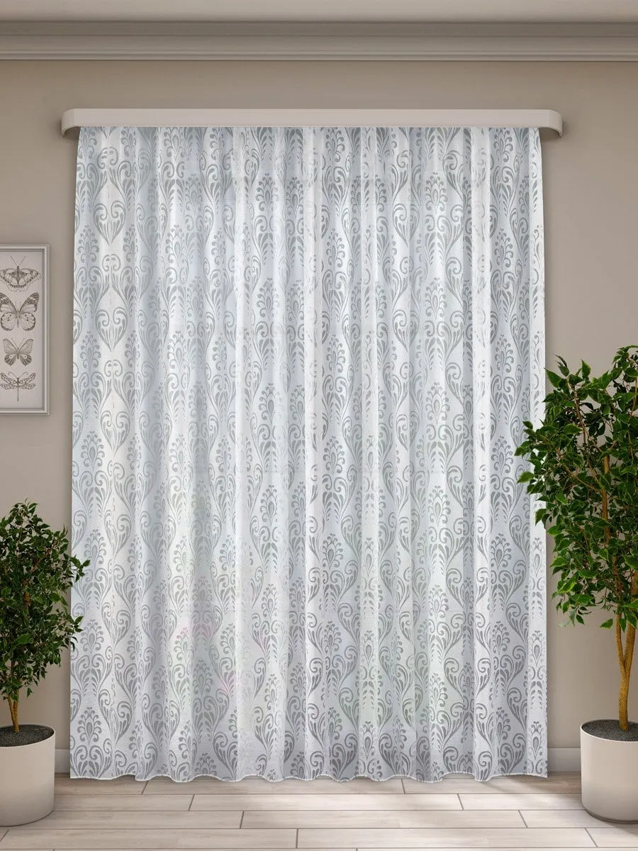 Elegant sheer curtain with silver floral lace pattern, softly diffusing daylight in a modern living room flanked by potted plants.