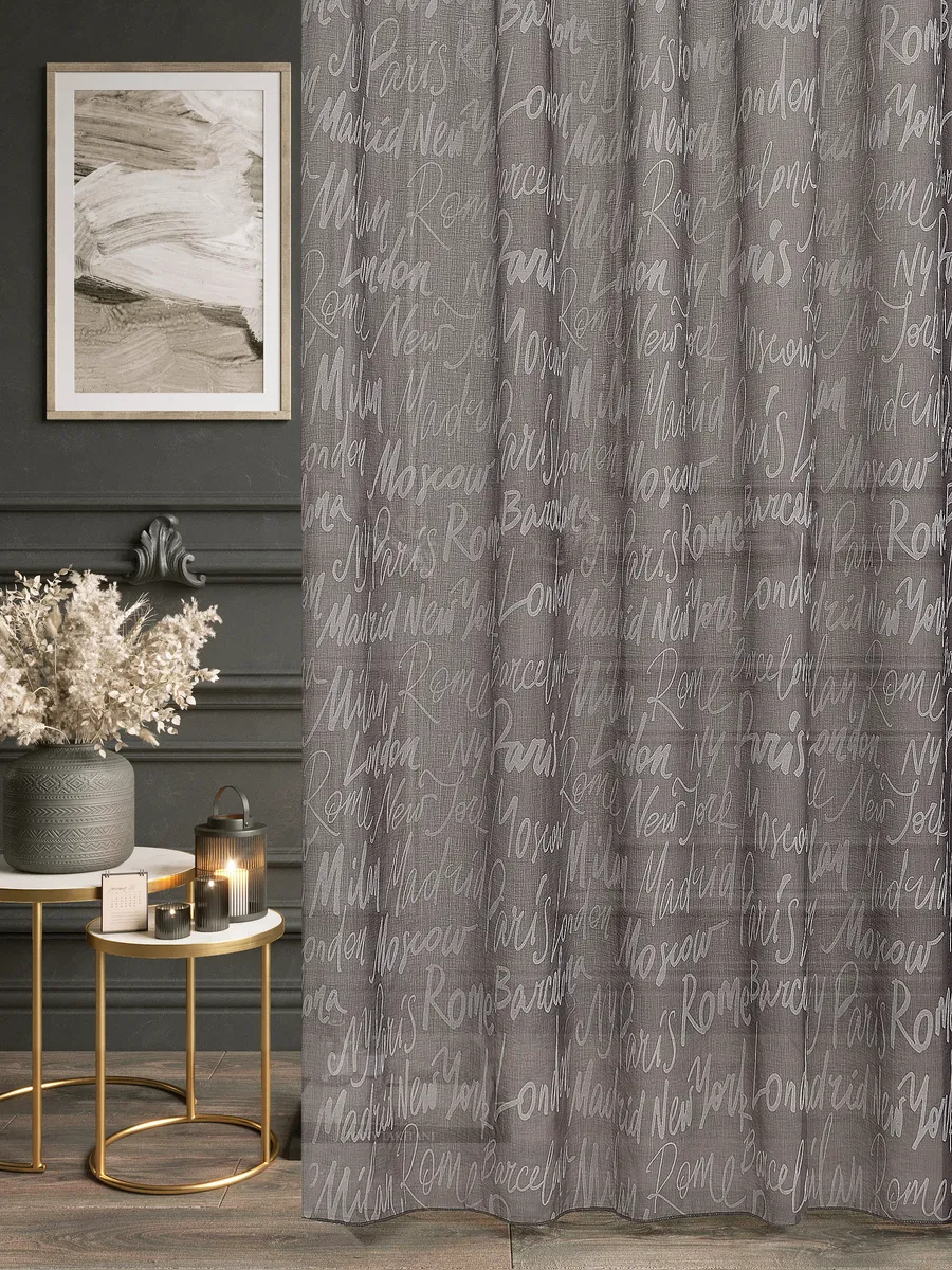 Тюль с узором городов в серых тонах висит на окне, мягко рассеивая свет. Интерьер с тёмными стенами, золотыми столиками и сухими цветами. Уютная атмосфера, тёплый свет свечи и современный декор.