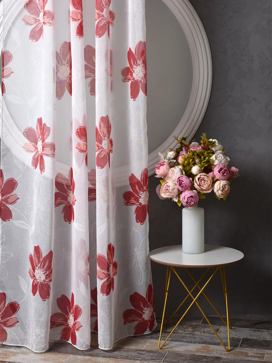 На фото — тюль с красными цветами висит у окна, рядом стоит столик с букетом роз. Интерьер с тёмной стеной и золотыми ножками стола. Ткань мягко колышется, пропуская дневной свет. Уютная атмосфера, наполненная нежностью и цветами.