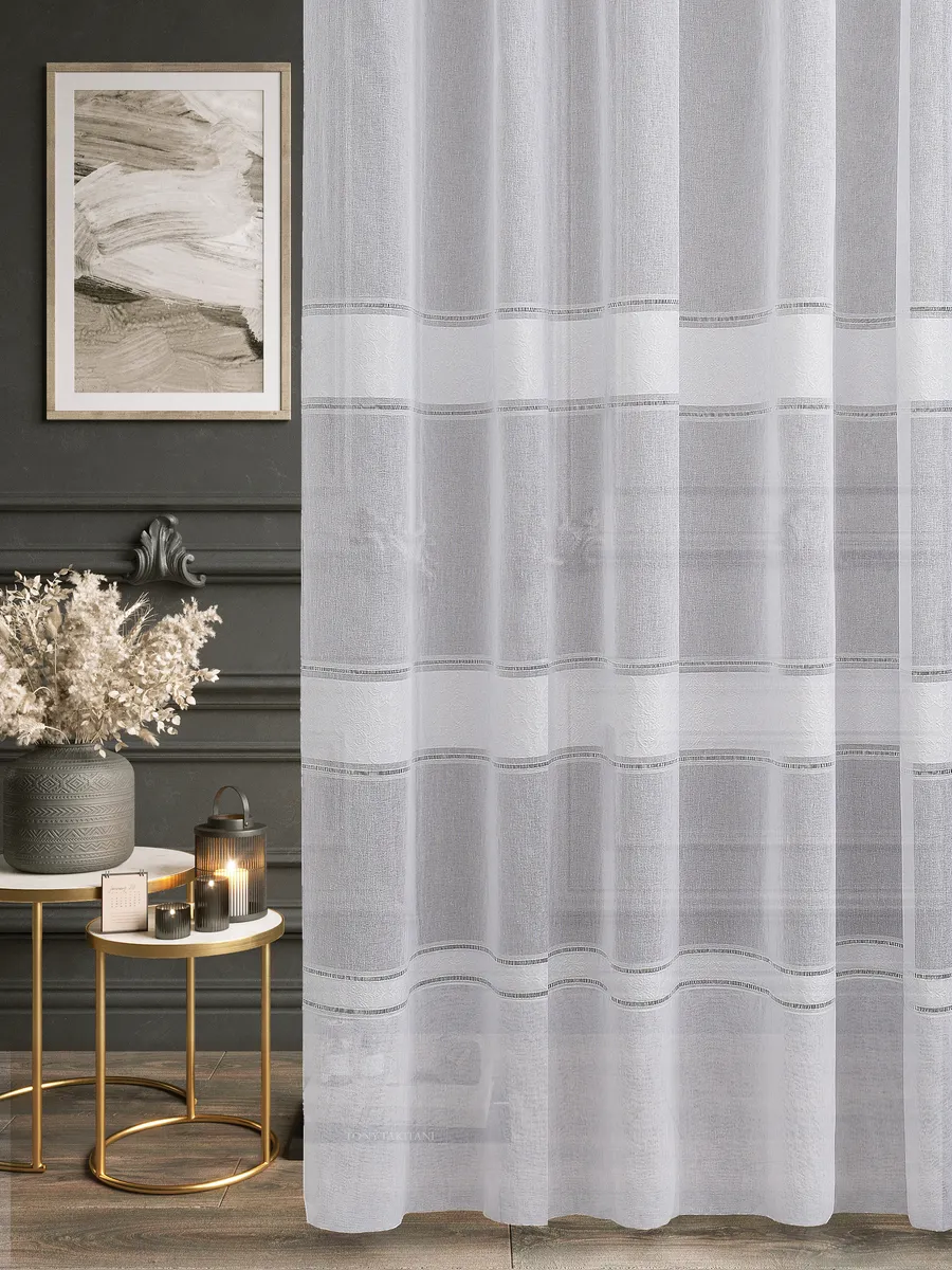 Прозрачный тюль с тонкими горизонтальными узорами висит на окне, пропуская рассеянный свет. На заднем плане — тёмная стена с картиной, золотые столики с лампой и сушёными цветами. Интерьер выглядит утончённо и уютно.