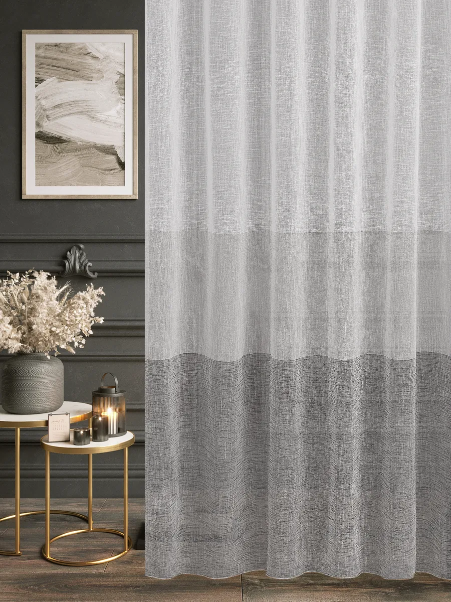 На фото — тюль с градиентом серого цвета, висящий в элегантном интерьере с тёмными стенами и золотыми столиками. Свет мягко проникает сквозь ткань, создавая уютную атмосферу. На заднем плане — картина в раме и сухоцветы в вазе.