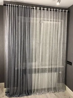 Modern geometric mesh curtain with grey and white grid pattern, softly diffusing daylight in a minimalist urban loft interior with light wood floors and grey walls.