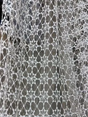 Воздушная сетчатая штора с геометрическим узором висит на окне, пропуская рассеянный свет. Интерьер выглядит уютно и современно. Ткань колышется, создавая игру света и тени.