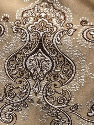 Роскошные шторы с вышитым вензелем в тёплых тонах, мягко падают на окно, пропуская рассеянный свет. Интерьер в стиле лофт с деревянными элементами. Узор напоминает старинную вышивку. Воздух уютный, атмосфера элегантная.