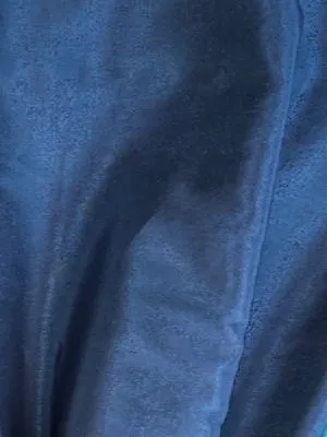 Тафта тёмно-синего оттенка с глубокими складками в элегантной комнате. Свет падает на ткань, подчёркивая её гладкость и сияние. Интерьер выглядит утончённо и роскошно.