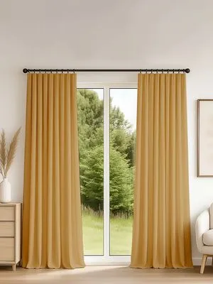 Тяжёлые шторы на ленте в тёплом золотистом оттенке, мягко драпируются на окне с видом на зелёный сад. Интерьер в нейтральных тонах, уютное освещение, деревянный пол, кресло и ваза с сухими растениями.