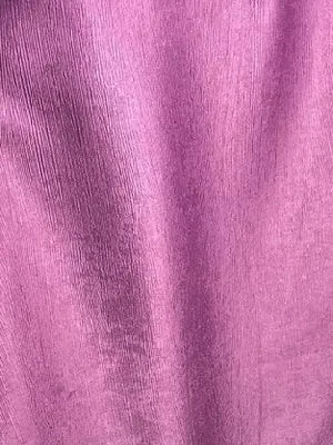 Текстурированная ткань розового оттенка висит на окне, мягко колышется от ветерка, создаёт уютную атмосферу в светлом интерьере с естественным освещением.