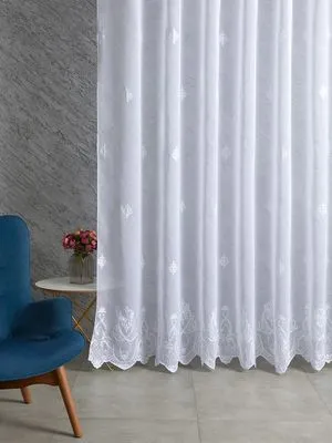 Лёгкий тюль с узором висит на окне, мягко пропуская свет. Слева — синий кресло и ваза с розами на столике. Стена — серый мрамор. Атмосфера умиротворённая и уютная.